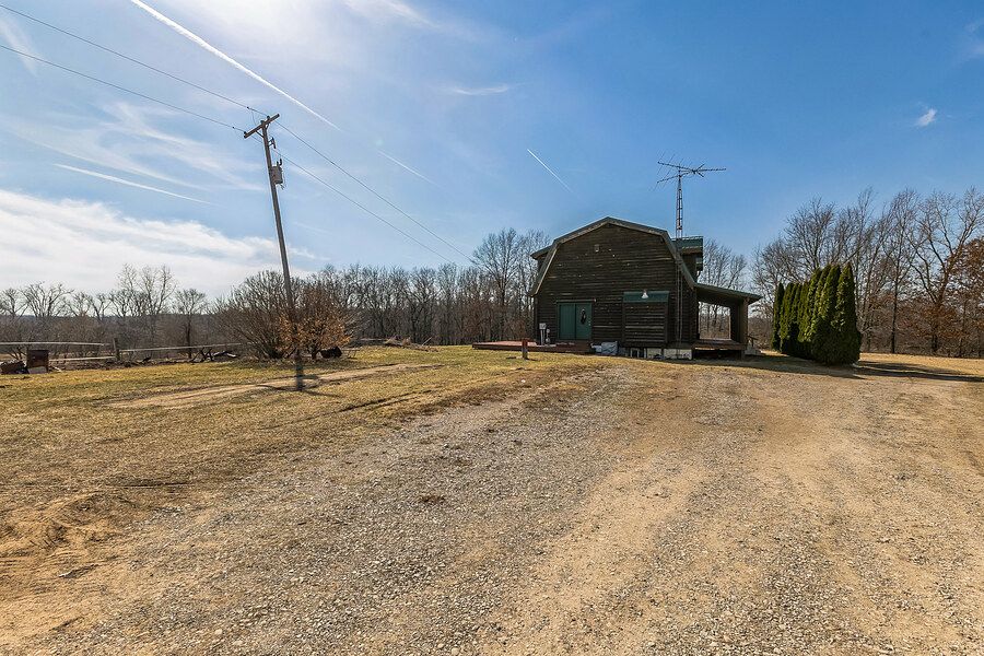 Gravel driveway leading to a rustic log cabin garage with carport and utility pole on rural property.
