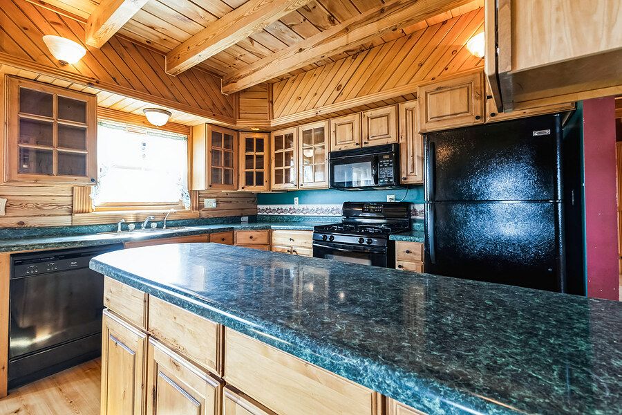 Log cabin kitchen featuring green granite countertops, oak cabinetry, black appliances, and wood ceiling.