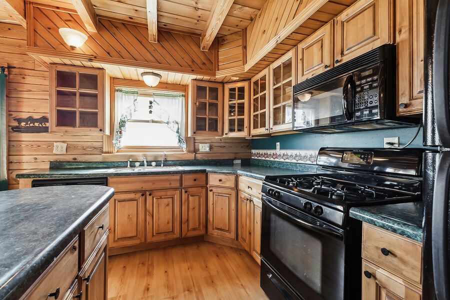 Rustic log cabin kitchen with wood cabinets, dark countertops, and black appliances.