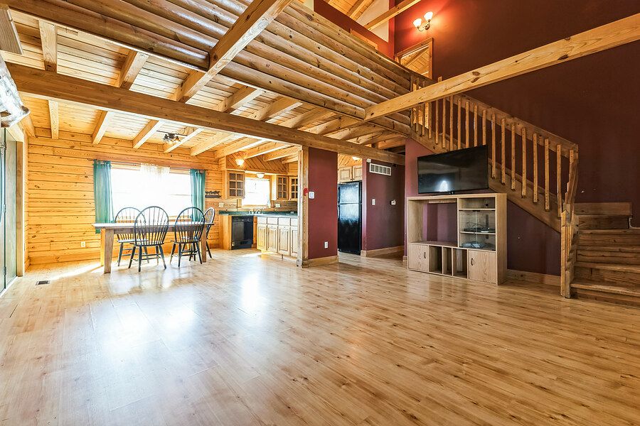 Spacious open-concept log cabin living area with hardwood floors, exposed beams, staircase, and kitchen view.