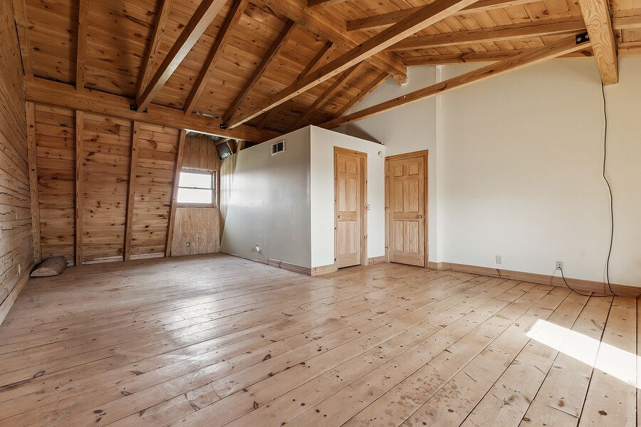 Empty room with vaulted wood beam ceiling, hardwood floors, and rustic wood-paneled walls with two doors.