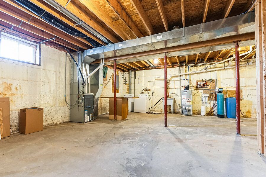Unfinished basement with exposed wooden beams, concrete floors, utility systems, and a small window allowing natural light.