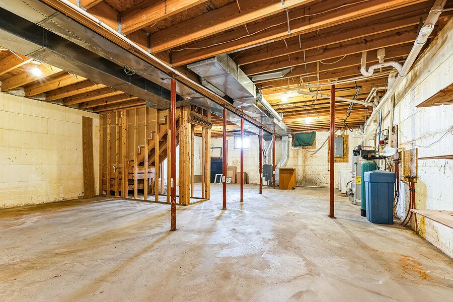 Unfinished basement with exposed wooden beams, concrete floor, support columns, and utility systems including water softener.