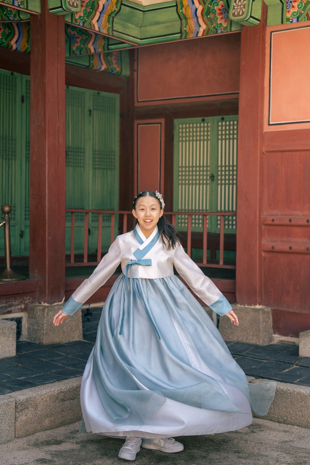 Young girl in traditional Korean hanbok dress twirling at a historic palace, smiling joyfully.
