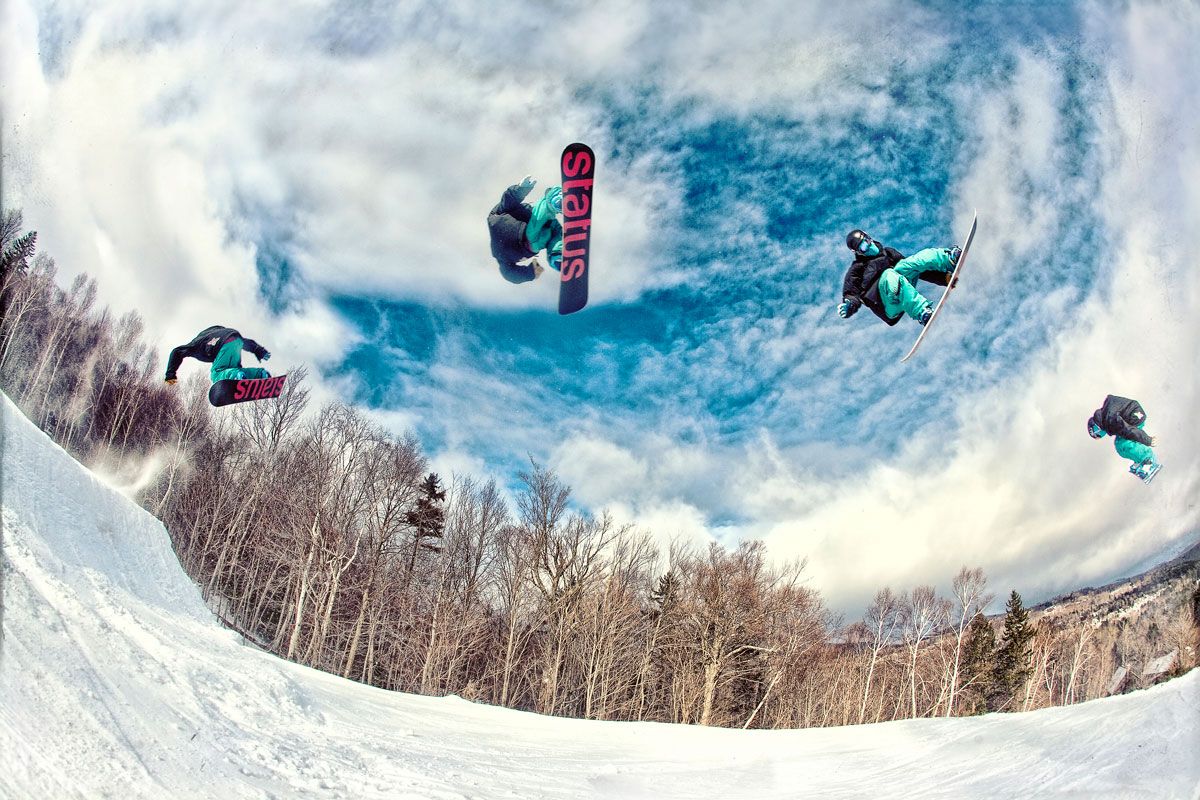 Snowboarder performing aerial tricks in a halfpipe with a sequence of jumps captured against a cloudy blue sky.