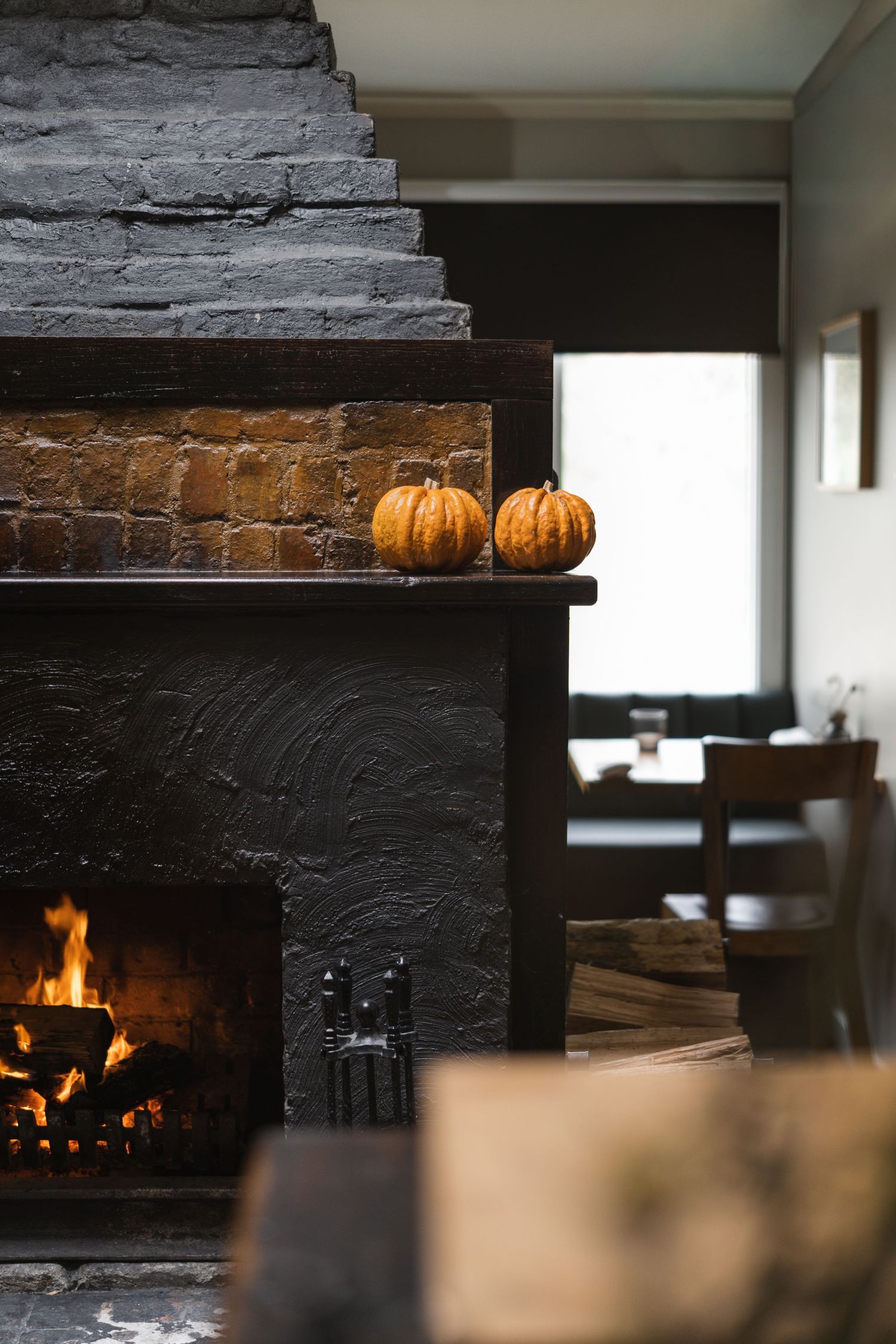 Black stone fireplace with two small orange pumpkins on the mantel with a warm glowing fire.

Surly Goat