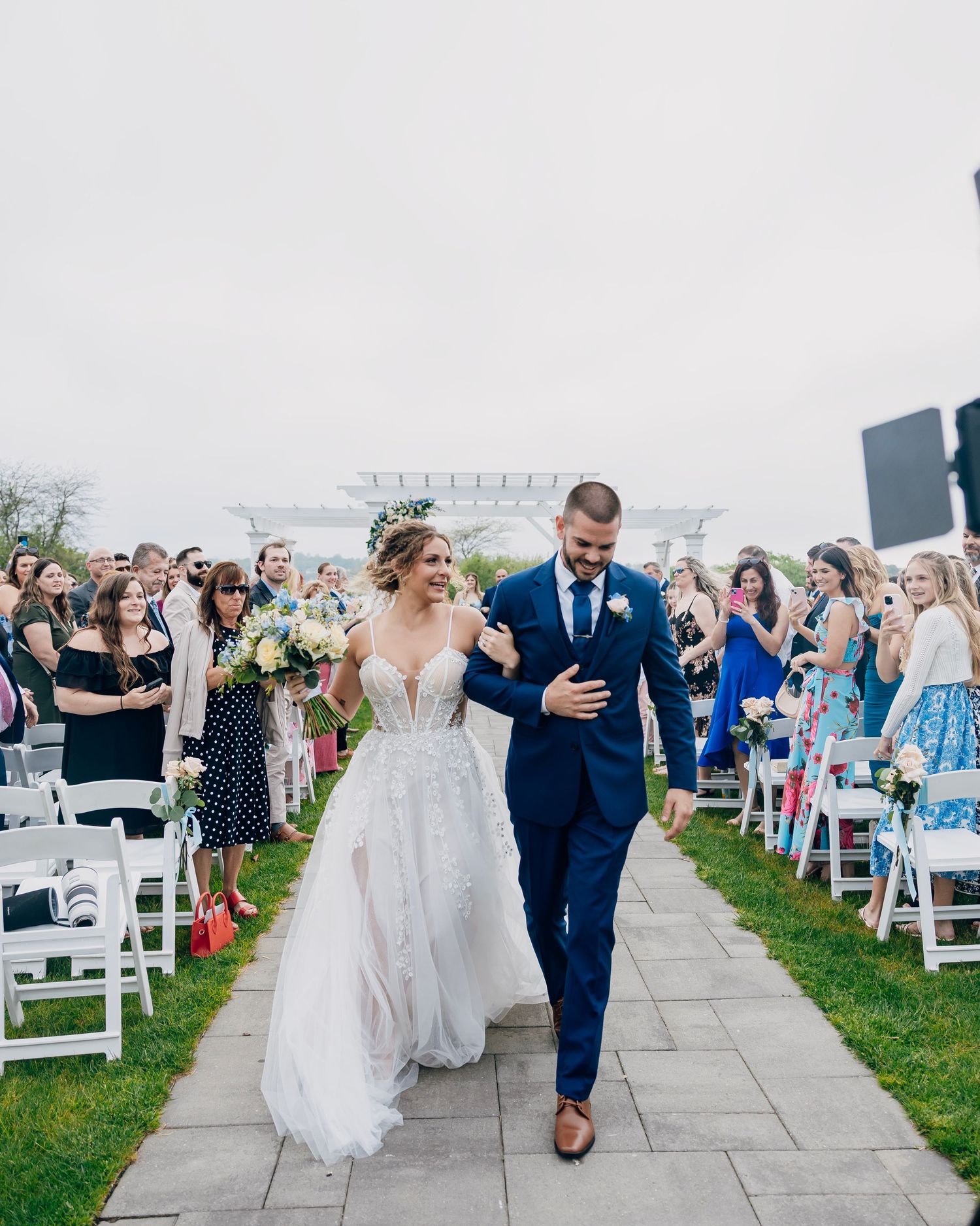 Bride and groom walk down outdoor aisle as guests celebrate their wedding ceremony.