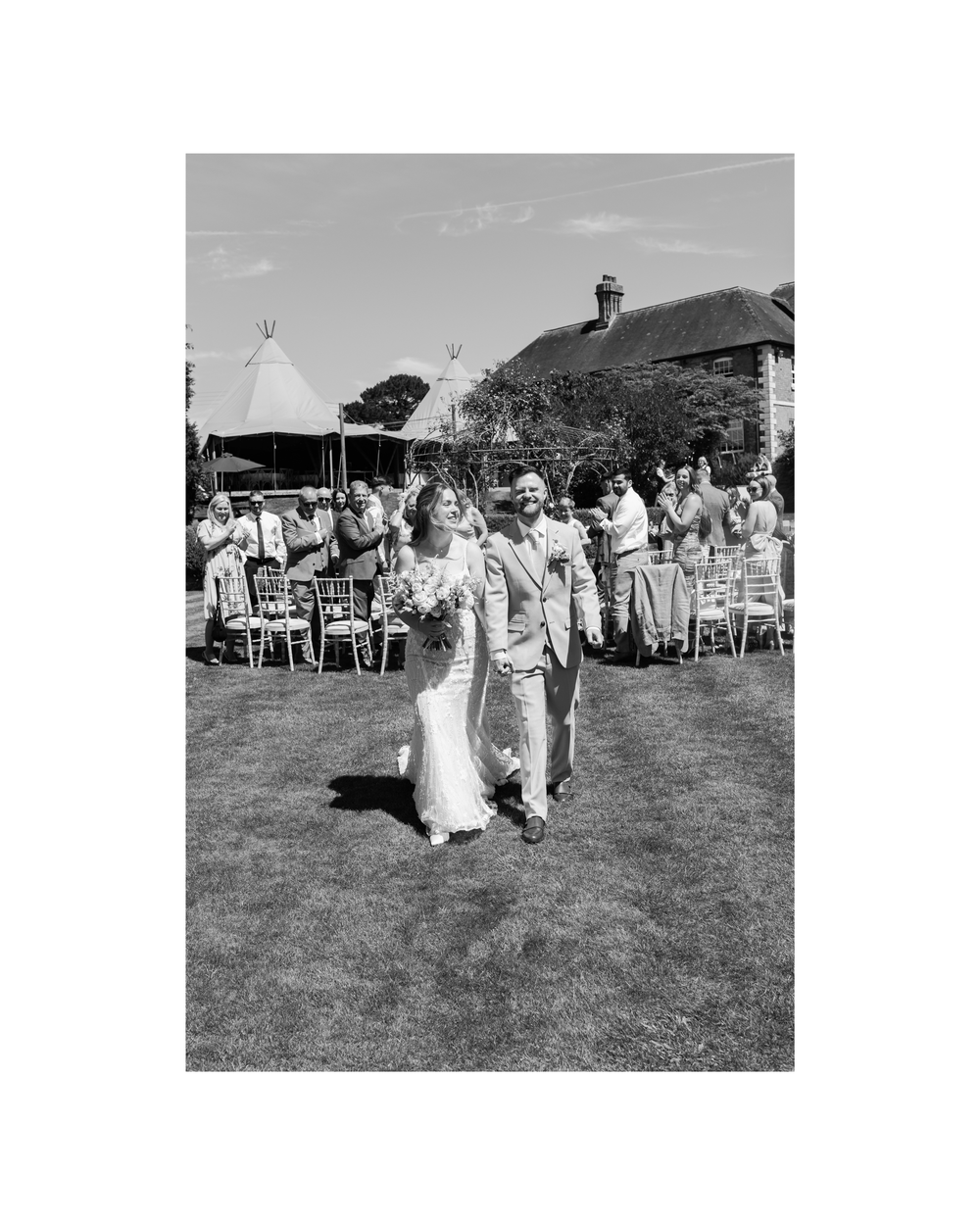 Black and white photo of a newlywed couple walking down the aisle at an outdoor wedding ceremony.