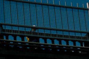 Person walking on a bridge overpass against a blue steel grid background in urban setting.