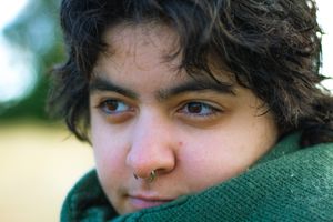 Close-up portrait of young person with nose ring wrapped in green scarf outdoors.