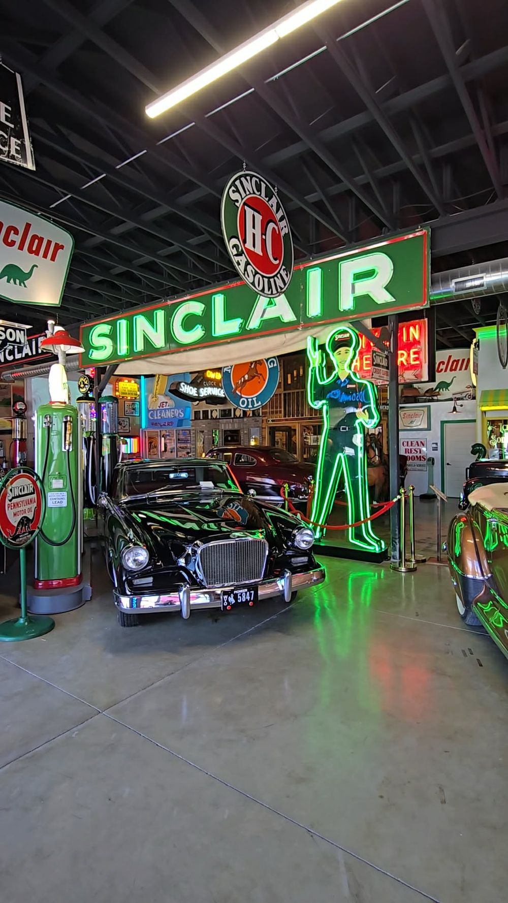 Vintage Sinclair gas station display with neon signs, classic black car, and retro memorabilia inside a museum exhibit.