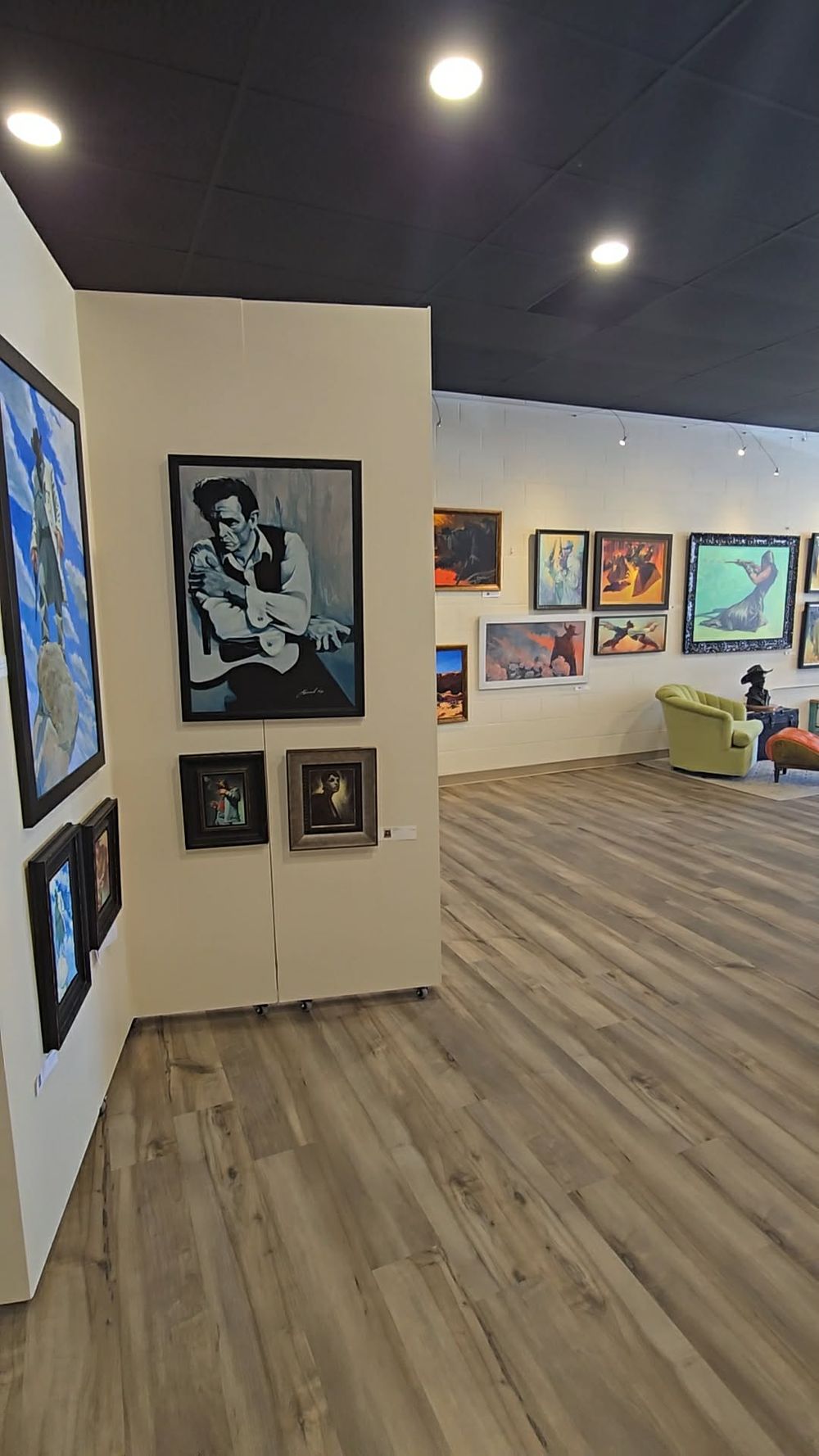 Modern art gallery interior with colorful paintings on white walls, hardwood floors, recessed lighting, and a cozy seating area.