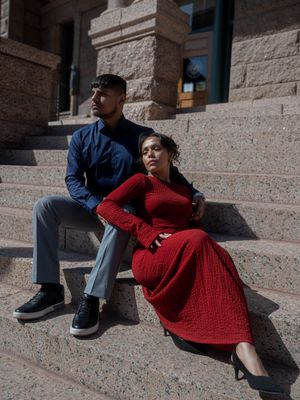 Stylish couple sitting on stone steps of a historic building, man in blue shirt and woman in red dress.