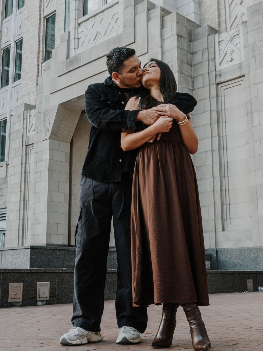 Couple sharing a tender embrace and kiss outside a grand white stone building with ornate architectural details.
