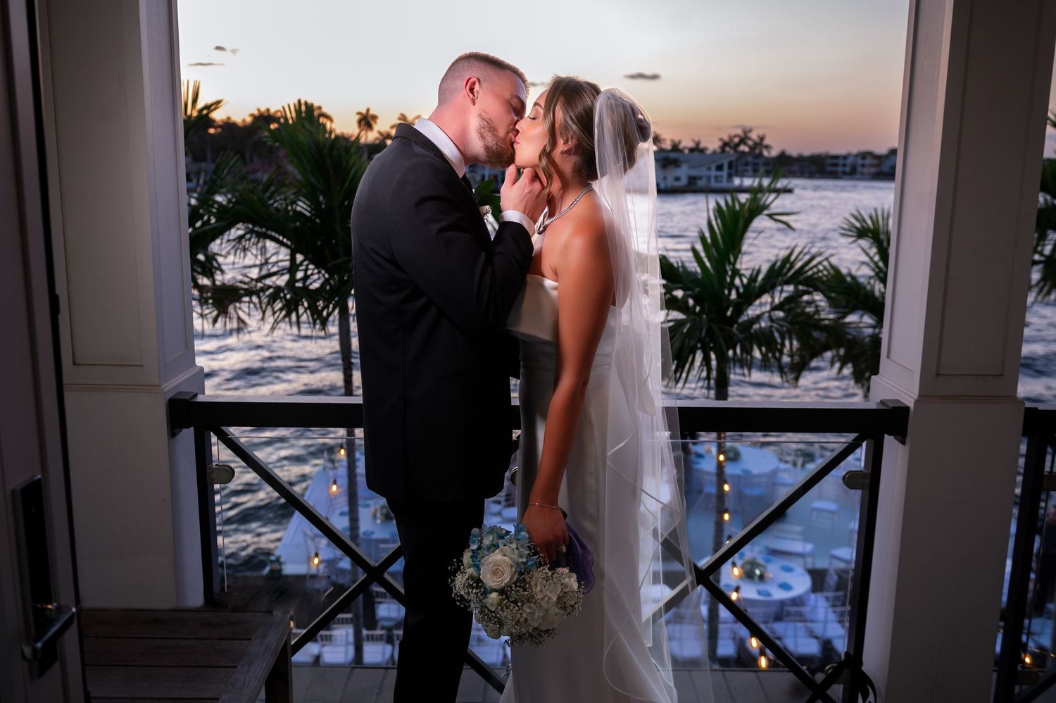 The groom kisses his bride on the balcony of their Treasure Coast estate wedding overlooking the water.