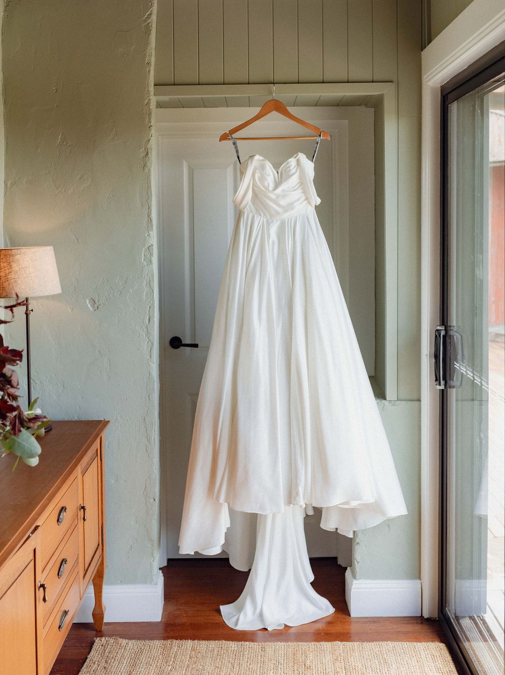 White wedding dress displayed on hangers in a minimalist room with natural lighting and wooden floors.