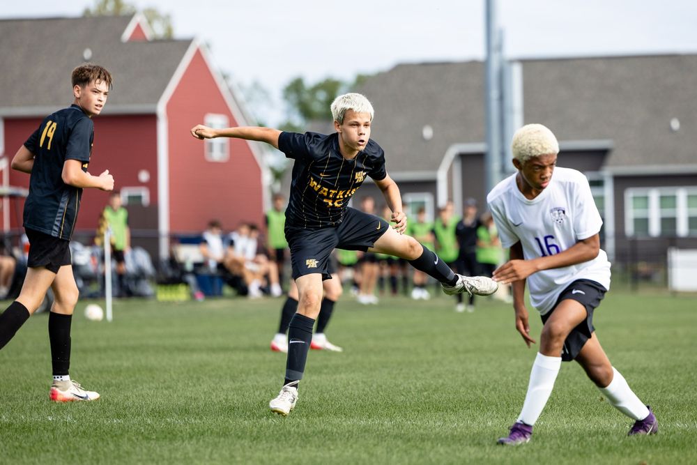 Soccer players in black and white uniforms compete for possession of the ball during an intense match on a grass field.