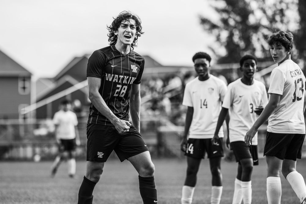 A soccer player in a black jersey reacts emotionally during a match while teammates look on in black and white photography.