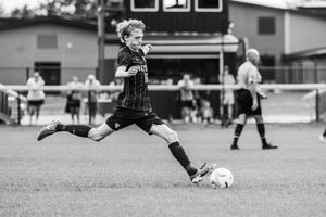 Soccer player in dark uniform makes a kicking motion during a match on grass field.