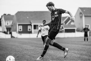 Black and white action shot of a soccer player kicking the ball during a match on a grass field.
