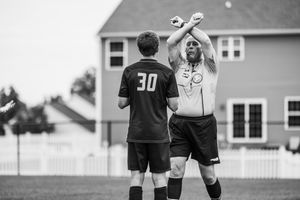 Soccer teammates celebrate together on the field during a match with a jumping high-five celebration.