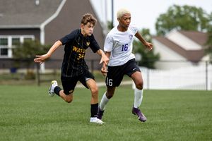 Two soccer players compete for possession of the ball during an intense match on a grass field.
