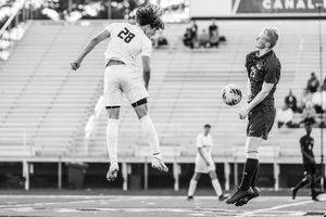 Black and white action shot of two soccer players competing for the ball during a match in a stadium.