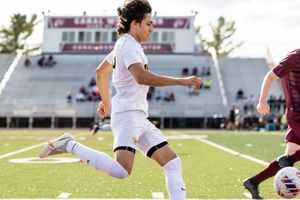 Soccer player in white uniform performs a sliding tackle against opponent in maroon jersey during competitive match.