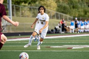 Soccer player in white jersey controls the ball during a competitive match on artificial turf field.