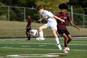 Soccer player in white jersey stretches to kick the ball during competitive match on turf field.