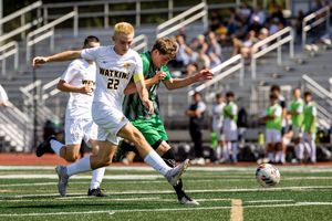 Soccer players compete for ball possession during match on sunny day at outdoor stadium.