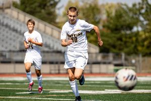 Soccer player in white uniform kicks the ball during competitive match on outdoor field.