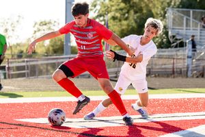 Soccer players compete for possession of the ball on a red turf field during an intense match.