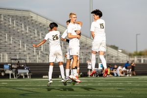 Soccer players in white uniforms celebrate together on a grass field during a match.