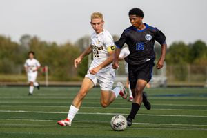 Soccer players in white and navy uniforms compete for possession of the ball during an outdoor match.