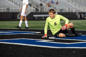 Soccer goalkeeper in neon yellow uniform diving to make a save on artificial turf.
