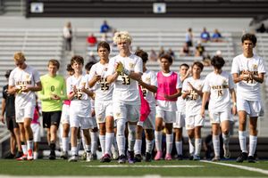 Soccer team members kneel in solidarity along the sideline during a pre-game ceremony.