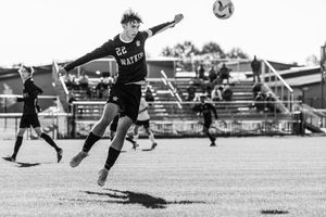 Soccer players dive and leap to block a ball during an intense match on a grass field.
