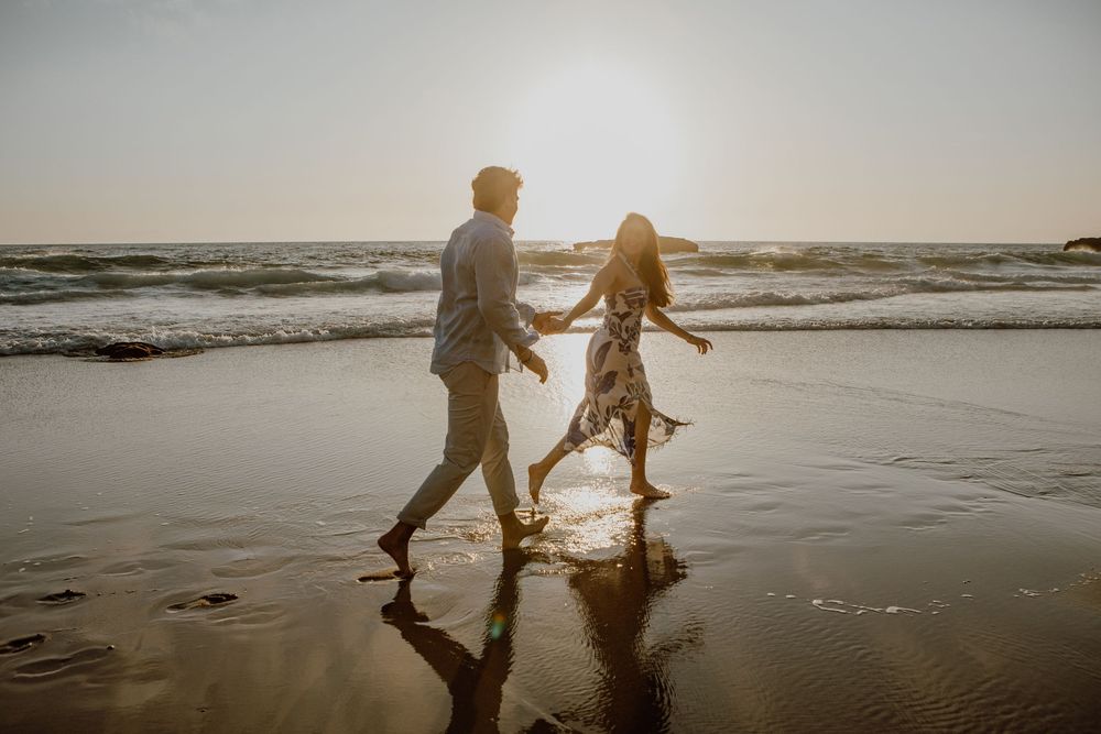 A couple dances together on a sunset beach as waves crash behind them creating a romantic silhouette.