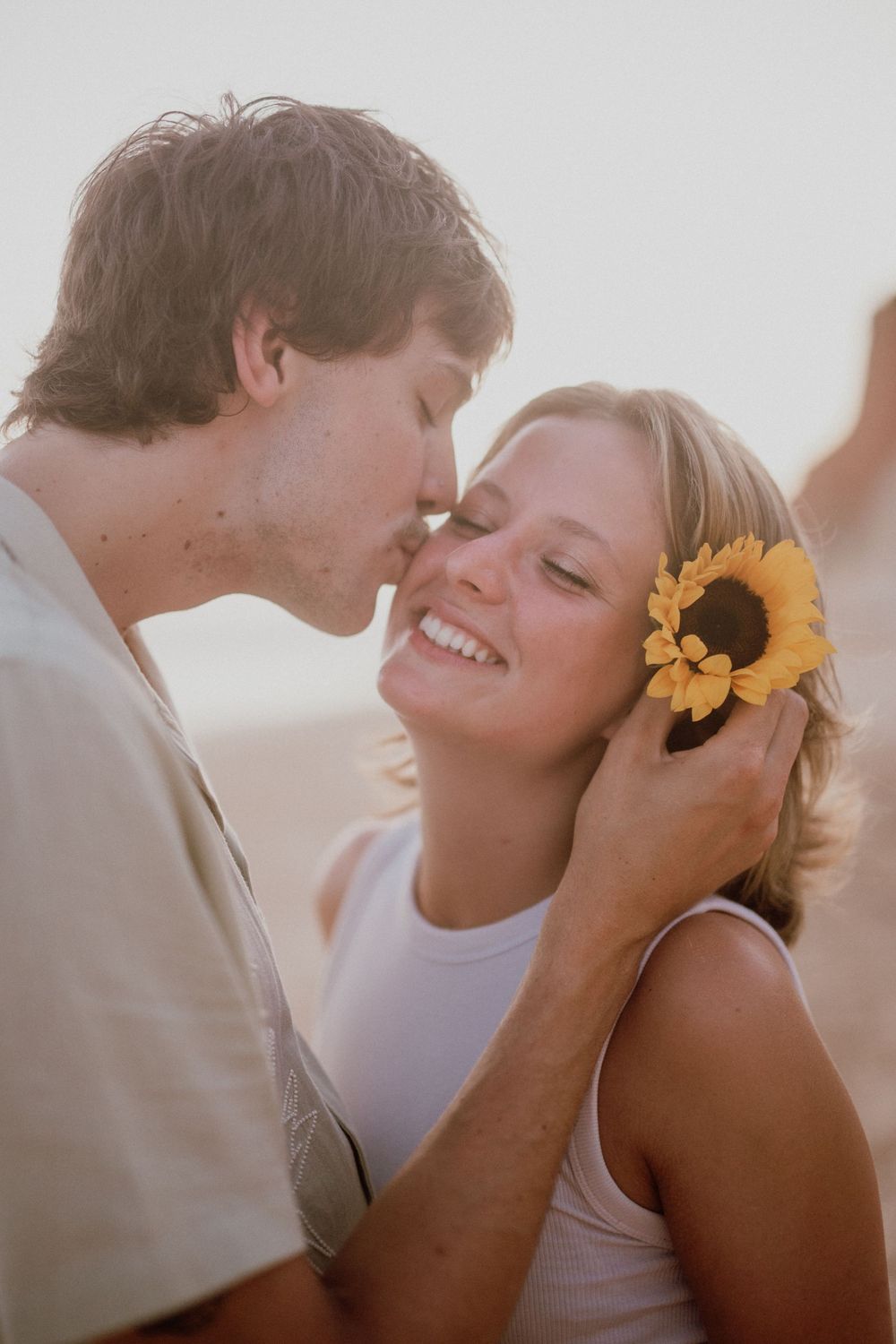 A romantic couple shares tender kisses at sunset while she wears yellow flowers in her hair.