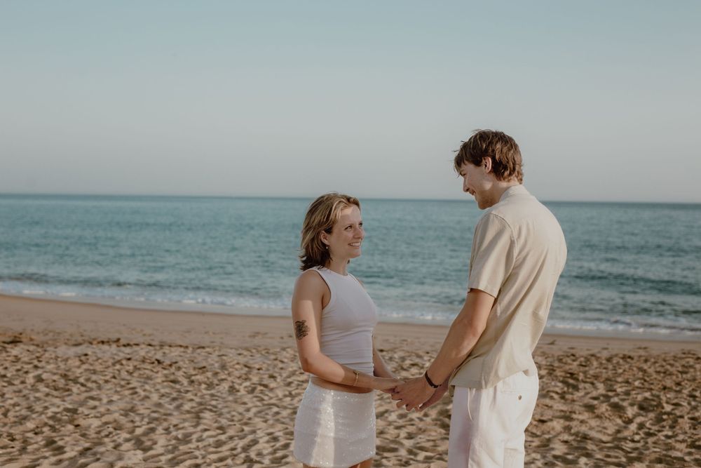 Romantic couple walking together on a sandy beach at sunset with ocean waves in the background.