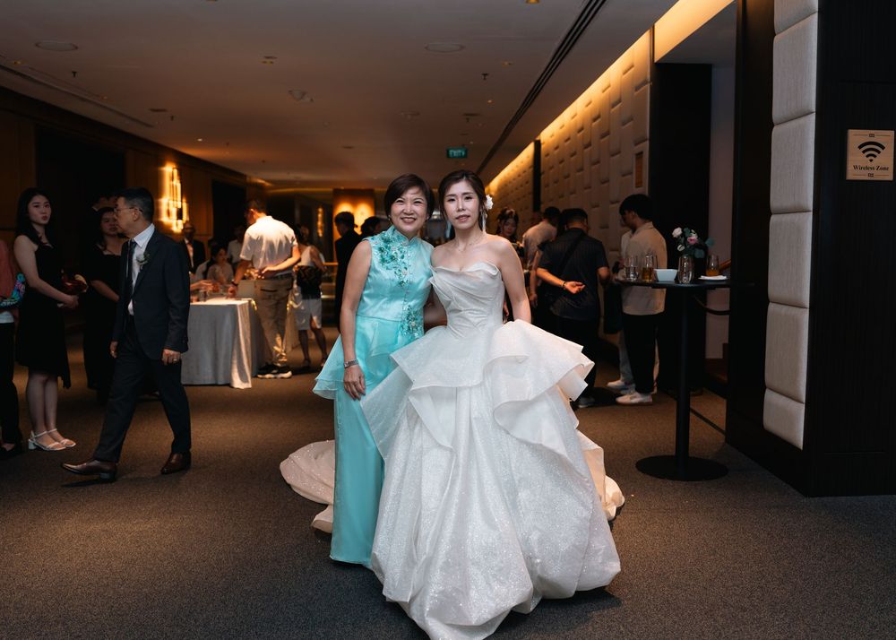 Wedding party members in aqua blue dresses and white gowns dance together in a dimly lit venue hallway.