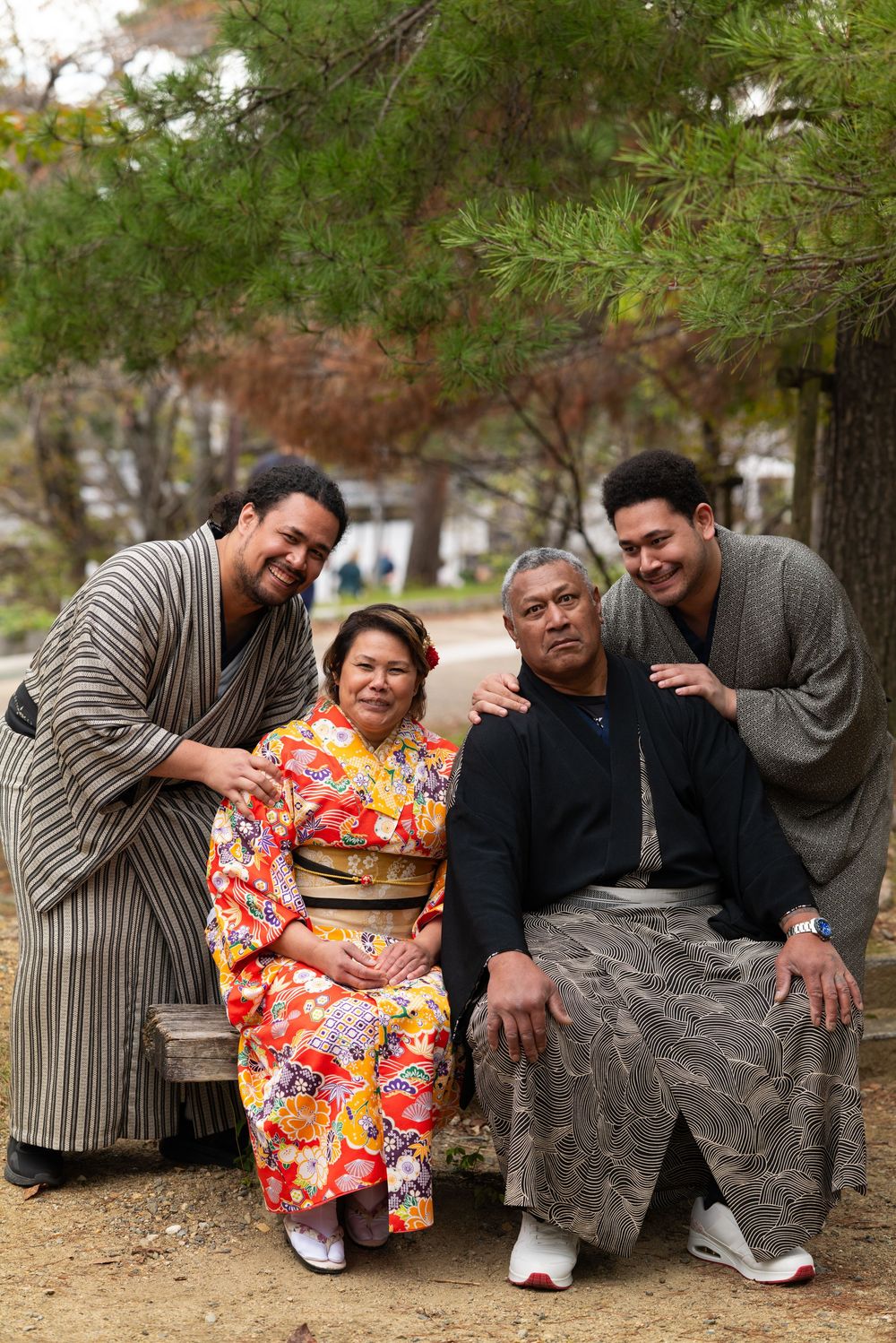 Happy family of four posing in kimono and yukata on a bench under a pine tree in Japan.