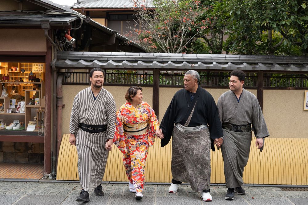 Family of four in traditional Japanese attire walking and smiling along a Kyoto street.