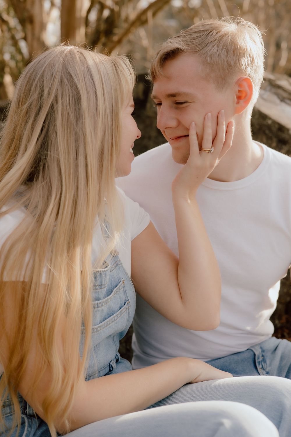 A tender romantic moment between a couple in casual denim and white clothing outdoors in warm sunlight.