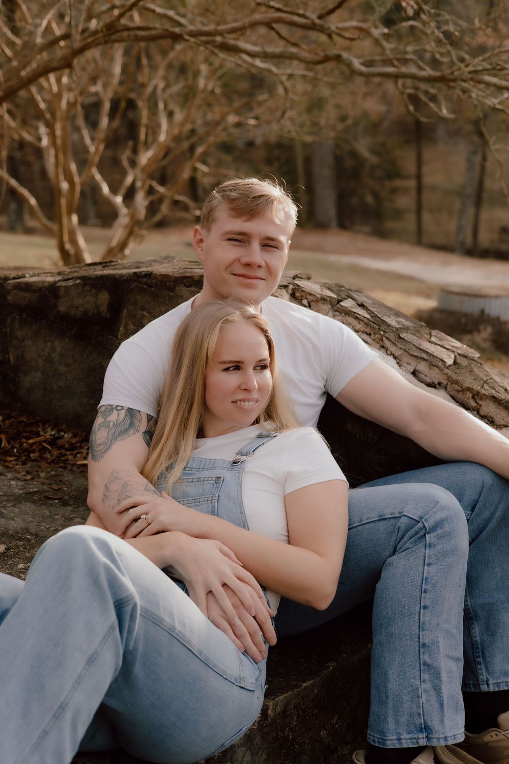 A couple in casual denim and white attire share tender moments while sitting together outdoors during a photo session.