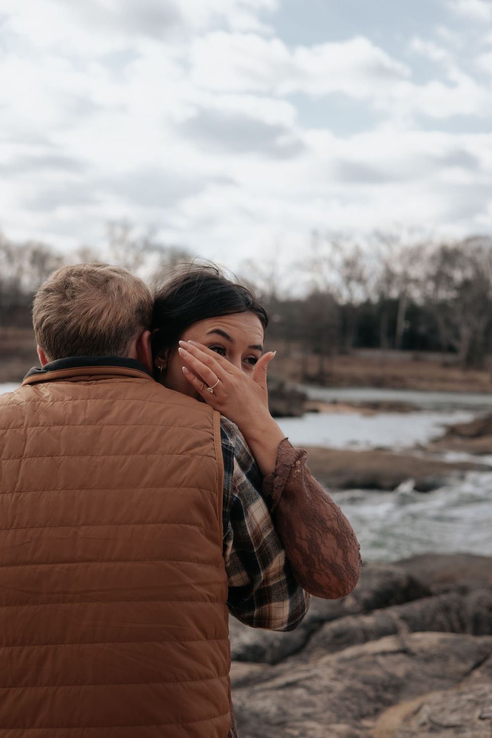 Two people share an intimate moment near a rocky stream on an overcast autumn day.