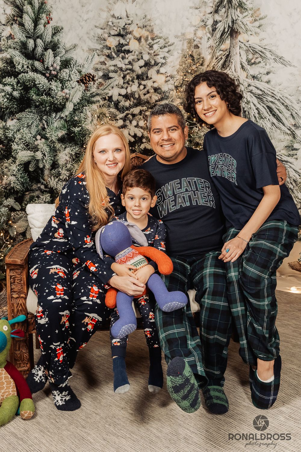 Family wearing matching Christmas pajamas sits together on couch with plaid blanket and winter decorations. Christmas Pictures Galveston