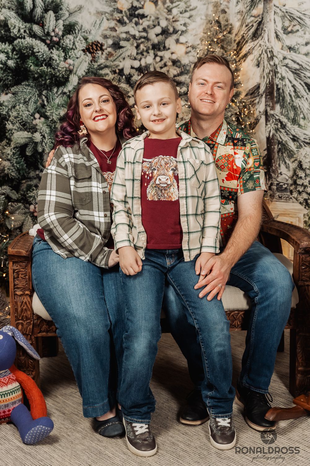 A family wearing plaid and denim poses together for a cozy winter holiday portrait with snowy decorations in the background. Webster
