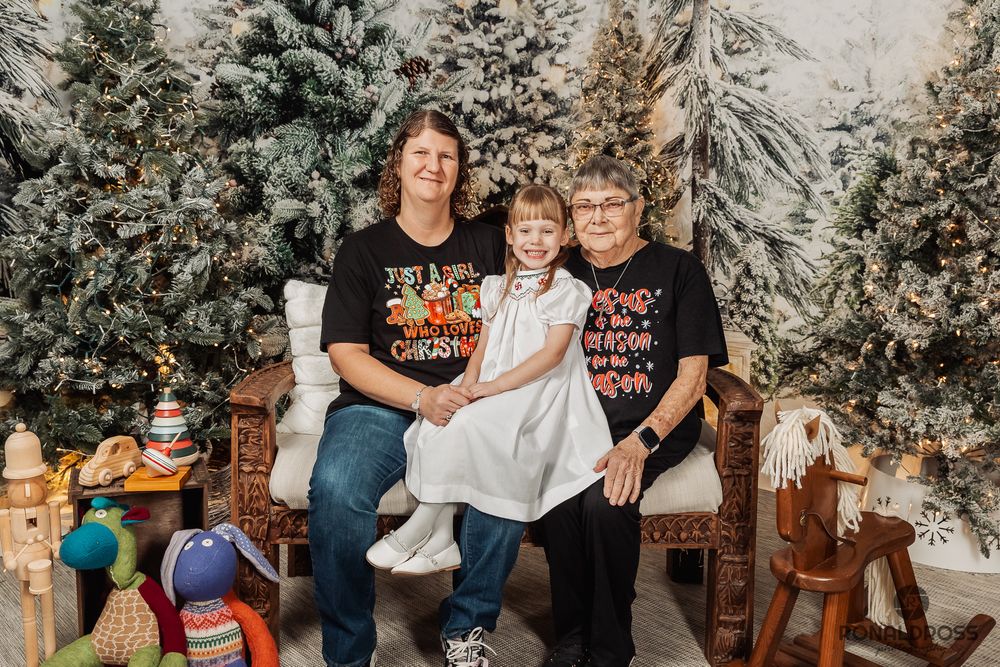 Two people wearing Halloween-themed shirts sit together on a wooden bench surrounded by snowy evergreen trees. Holiday Photos Galveston